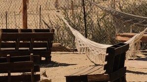Escena de playa con estructuras de madera, una hamaca y un vehículo en la arena.