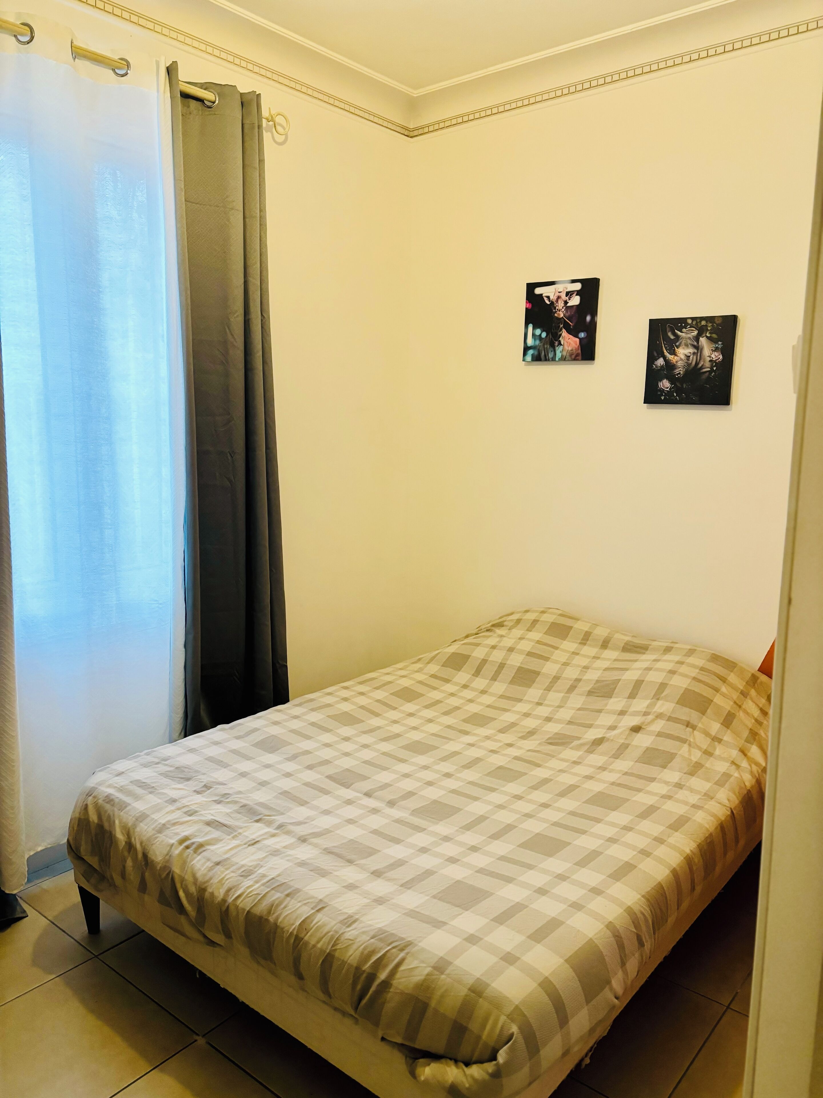 Un dormitorio con una cama, un ventanal con cortinas y dos cuadros colgados en la pared.
