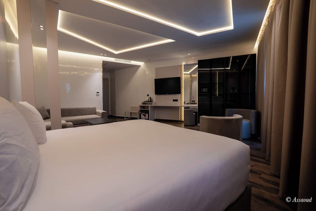 A modern hotel room with a large bed, a sofa, a desk, and a TV.