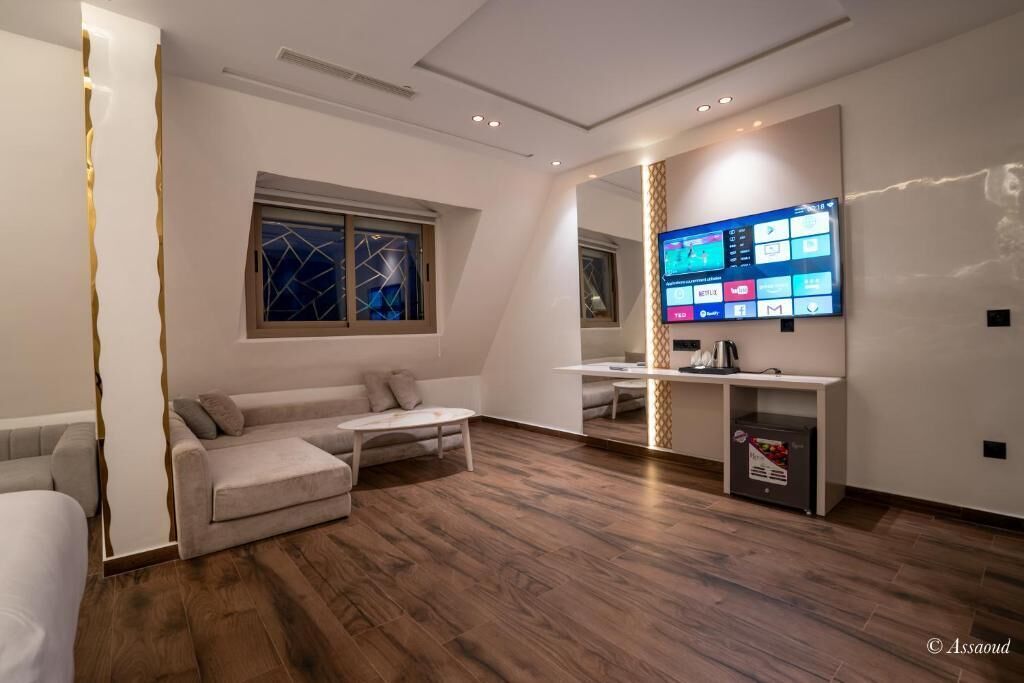 A modern living room with a large flat-screen TV mounted on the wall, a sofa, a coffee table, and a small kitchen area with a microwave.