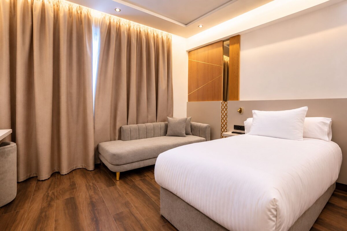 A hotel room with a large bed, a sofa, and a nightstand.