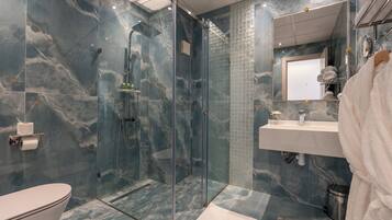 Un baño moderno con ducha envuelta en vidrio, paredes de mármol, lavamanos blanco y un espejo grande.