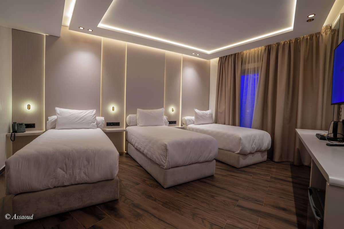 A hotel room with three beds, a desk, and a TV.
