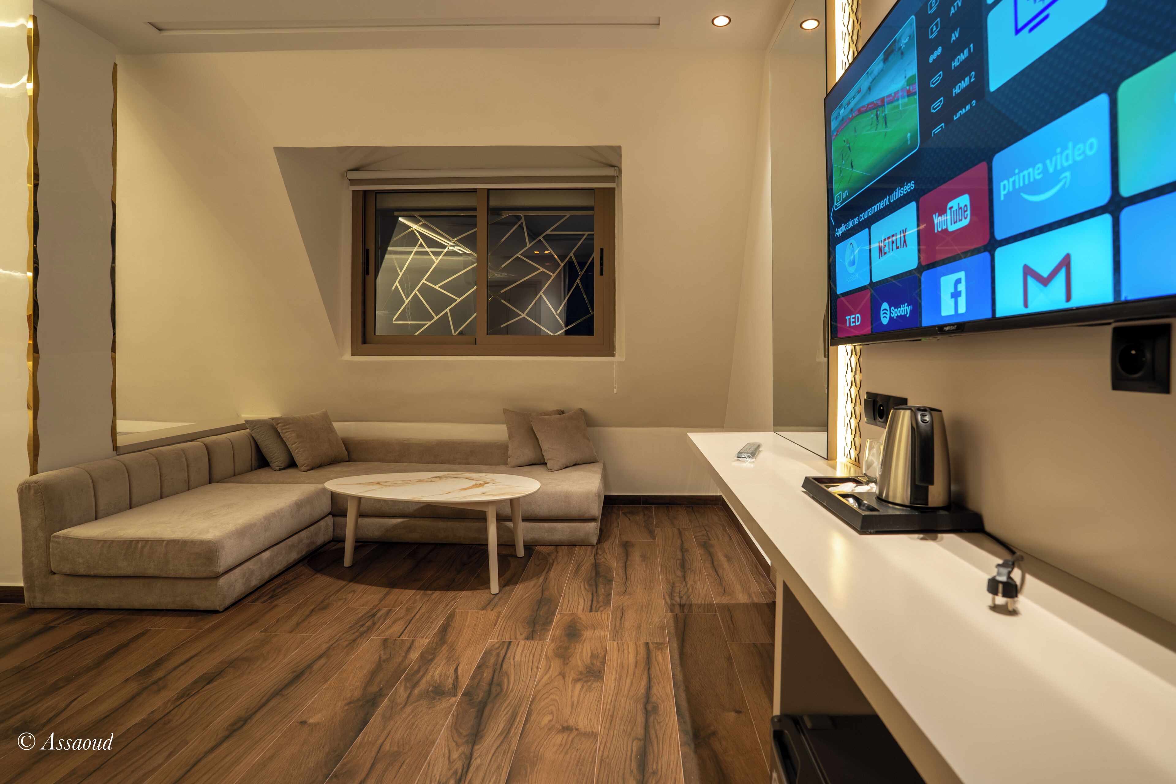 Ein modernes Wohnzimmer mit einem Ecksofa, einem Couchtisch und einem Flachbildfernseher, der verschiedene Streaming-Dienste anzeigt.