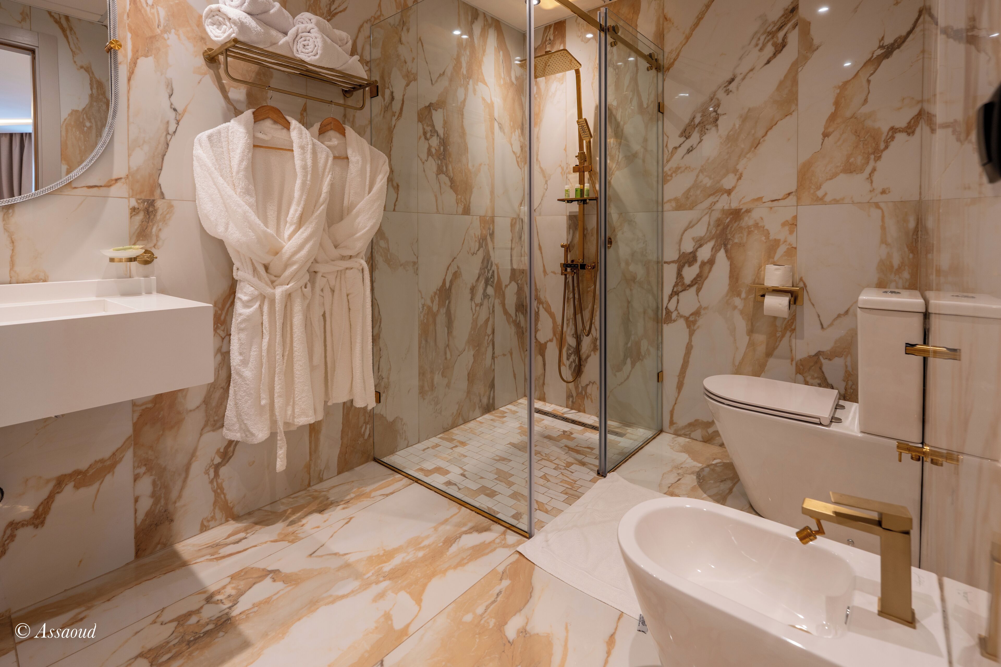 Une salle de bain aux murs recouverts de marbre, avec une douche en verre, un lavabo blanc et une baignoire.