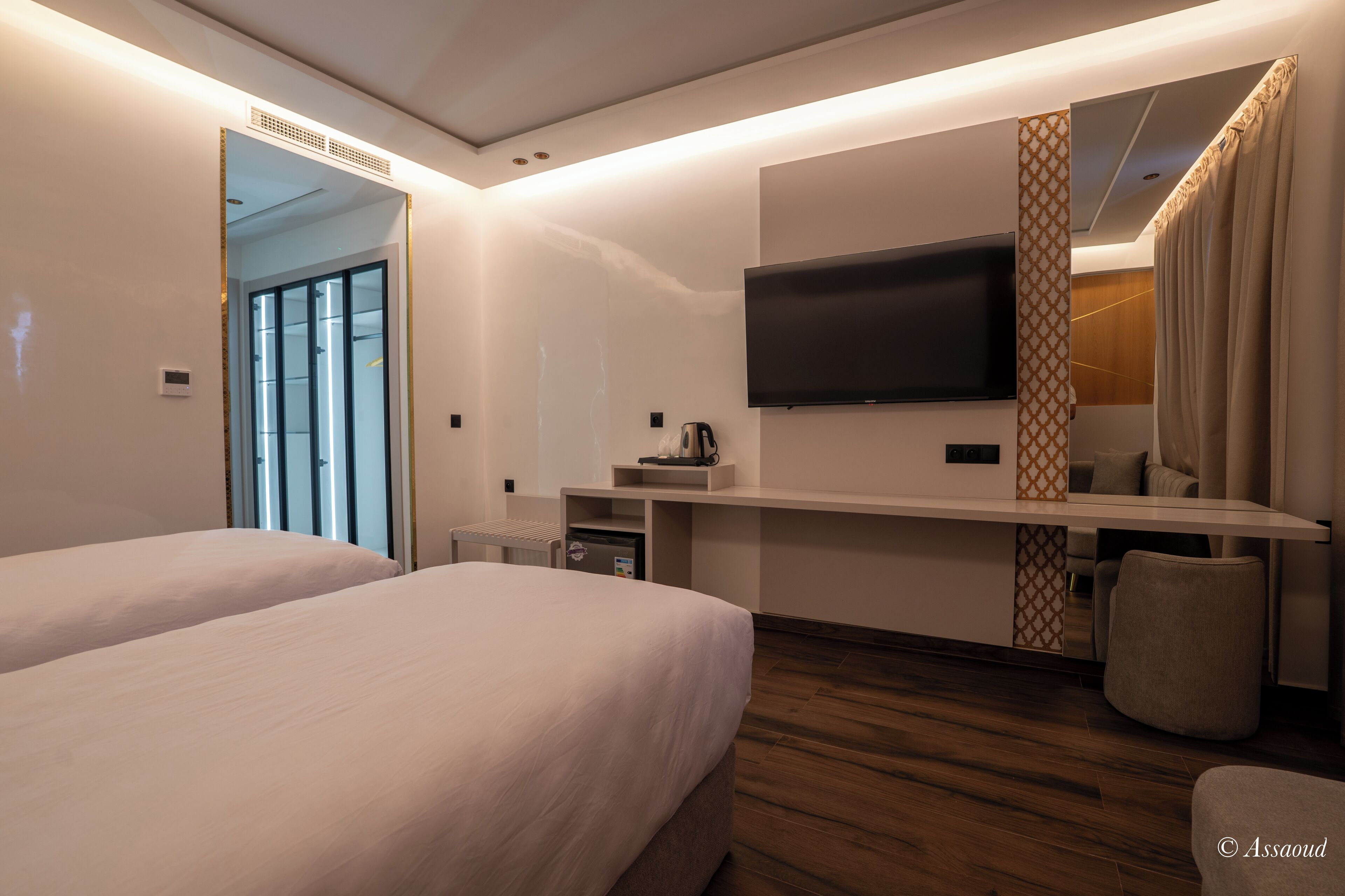 Una habitación de hotel moderna con dos camas, un televisor de pantalla plana en la pared, una kitchenette pequeña y un ventanal grande.