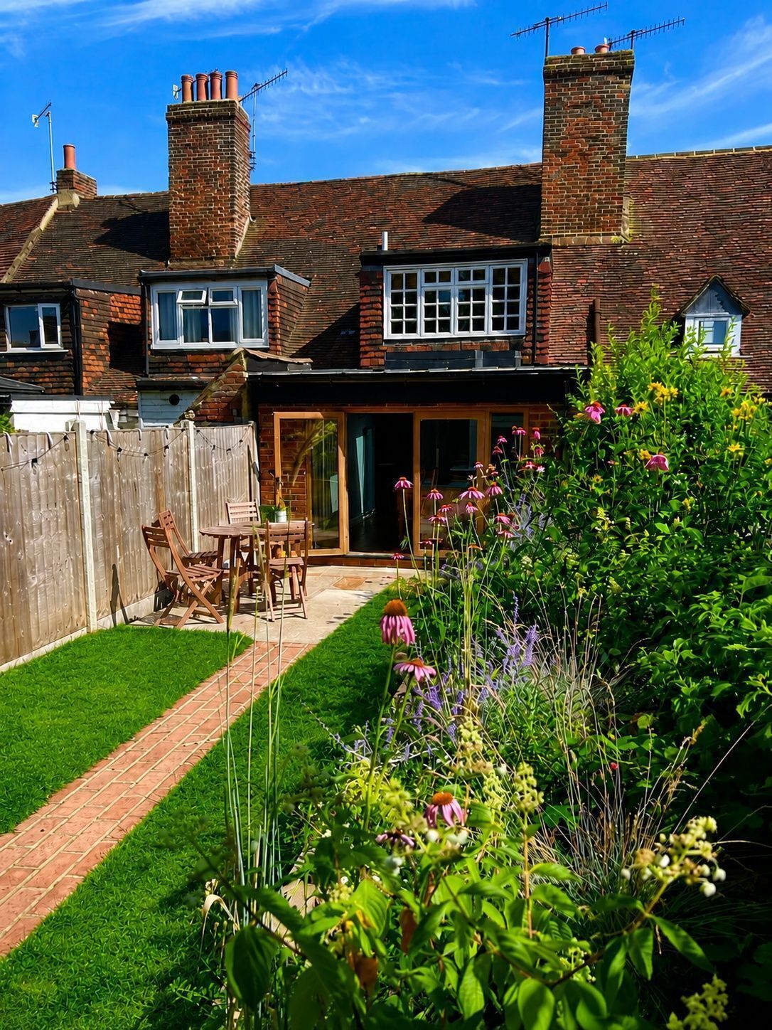 A residential property with a brick house, a fenced backyard, and a garden with various plants and flowers.