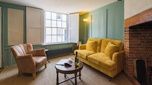 Quarto com poltrona de couro, sofá amarelo, mesa pequena com garrafa e copo, e lareira de tijolos.