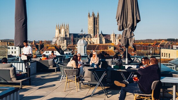 Terraço no telhado com área de estar ao ar livre, um garçom e vista para edifícios históricos.