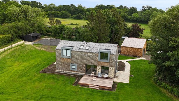 Une maison moderne à deux étages, dotée d’une terrasse et entourée d’une végétation luxuriante et d’une pelouse bien entretenue.