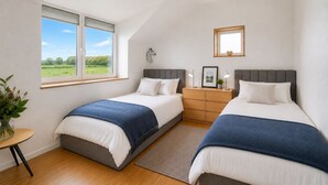 Une chambre avec deux lits, une table de chevet, une commode, une fenêtre donnant sur un beau paysage et un luminaire au plafond.