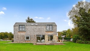 Une maison moderne à deux étages, avec une façade en pierre, de grandes fenêtres et une pelouse bien entretenue.