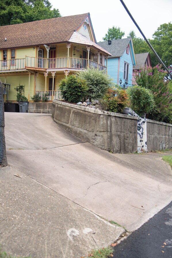 A two-story house with a balcony, a stone retaining wall, and a driveway leading to the front door.