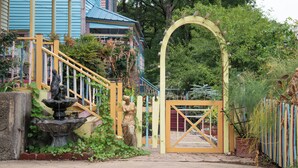 A garden with a fountain, a statue, and a gate leading to a house with a blue exterior. - Miss Scarlet 3-bedroom cottage in Historic downtown Hot Springs (Hot Springs)