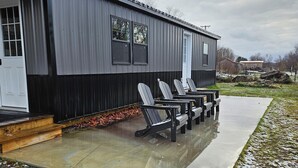 A building with a covered patio area, outdoor seating, and a concrete pathway. - Wonderful 1-bedroom cabin with AC in charming Potsdam on a brook. (Potsdam)