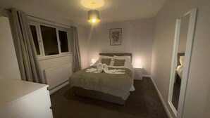 Et hotelværelse med seng, natbord, lampe og et vindue med gardiner.