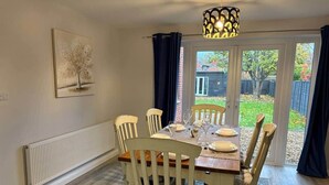 Et spiseområde med et bord dækket til fire personer, hvide stole, en radiator og udsigt ud gennem en glasdør.