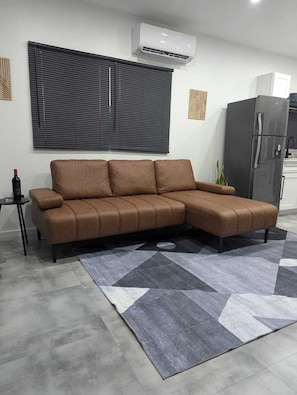 A brown sectional sofa with a geometric patterned rug, a wall-mounted air conditioner, and a refrigerator in a modern kitchen setting. - Modern Cottage with Pool  in Cedar Valley (Cedar Valley)