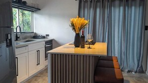 Eine moderne Küche mit einer zentralen Kochinsel, einem Essbereich mit einer Bank und einem Fenster mit Jalousien.