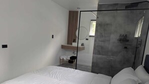 A modern bedroom with a large bed, a glass shower enclosure, a small vanity with a mirror, and a window providing natural light. - Modern Cottage with Pool  in Cedar Valley (Cedar Valley)