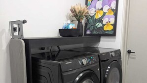Ein kompakter Waschraum mit zwei schwarzen Samsung Frontlader-Waschmaschinen, einer kleinen schwarzen Ablage mit Dekoration und einem gerahmten Blumenbild an der Wand.