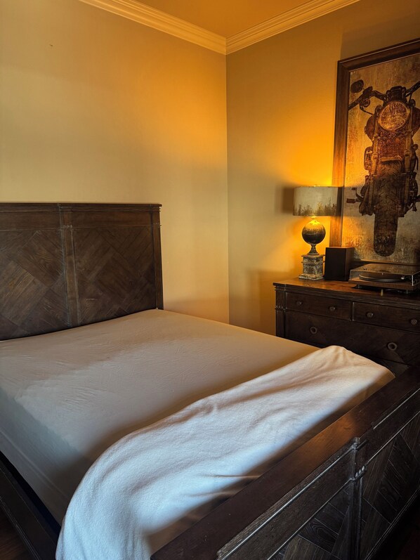 A neatly made bed in a room with a wooden headboard, a lamp on a wooden nightstand, and a framed picture on the wall. - Family Holiday Rental (Baton Rouge)