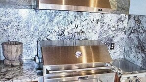 A kitchen with a stainless steel range hood, a built-in grill, and a wooden cabinet base. - Family Holiday Rental (Baton Rouge)
