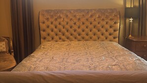 A bedroom with a tufted headboard, a patterned bedspread, and a window with curtains. - Family Holiday Rental (Baton Rouge)