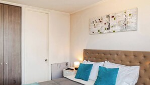 A neatly arranged bedroom with a large bed, a bedside table, a nightstand, and a wardrobe. - Apartment in Metro U. de Chile with Balcony, Gym & Swimming Pool, Historic Center Santiago (Santiago)