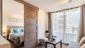 A modern hotel room with a large bed, a desk, and a view of the city through large windows. - Apartment in Metro U. de Chile with Balcony, Gym & Swimming Pool, Historic Center Santiago (Santiago)