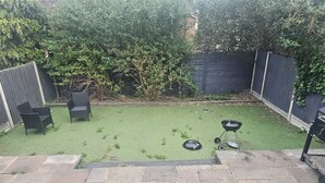 A backyard with artificial grass, two wicker chairs, a barbecue grill, and a stone-tiled patio. - River View Flat, 5 minutes Drive to Bluewater and Greenhithe Station (Greenhithe)
