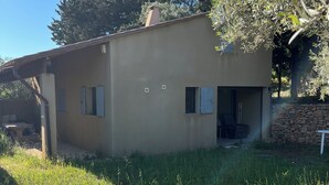 A single-story building with a flat roof, a stone wall in the foreground, and a grassy area in the foreground. - Small, quiet house (Ollioules)