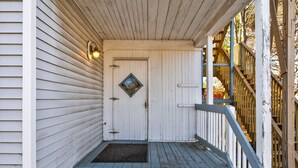 A wooden porch with a white door, a small window, and a metal step leading up to the entrance. - The Coastal Connection (South Portland)