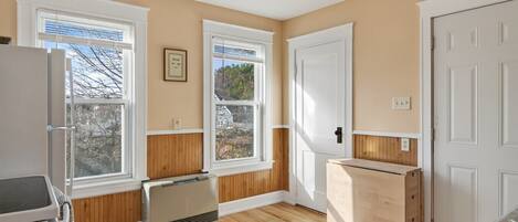 Una cocina con pisos de madera, gabinetes blancos, horno empotrado y ventana con vista a árboles.