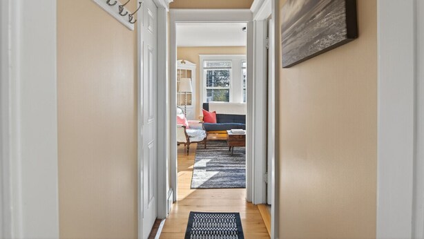 A hallway leading to a living room with a sofa, a lamp, and a window. - The Coastal Connection (South Portland)
