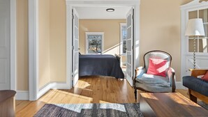 A room with a bed, a chair, a lamp, and a view of a staircase leading to another room. - The Coastal Connection (South Portland)