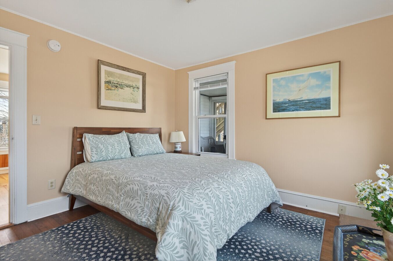 A bedroom with a bed, a nightstand, a lamp, a window, and a door.