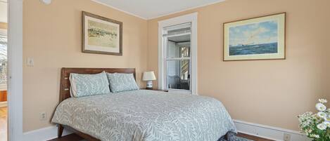 A bedroom with a bed, a nightstand, a lamp, a window, and a door.