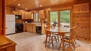 Una cocina de cabaña de madera con una mesa de comedor y sillas, un refrigerador, estufa y un lavabo.