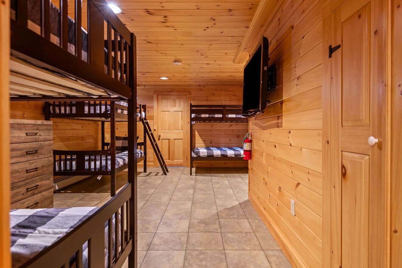A wooden cabin with bunk beds, a fire extinguisher, and a television on the wall.