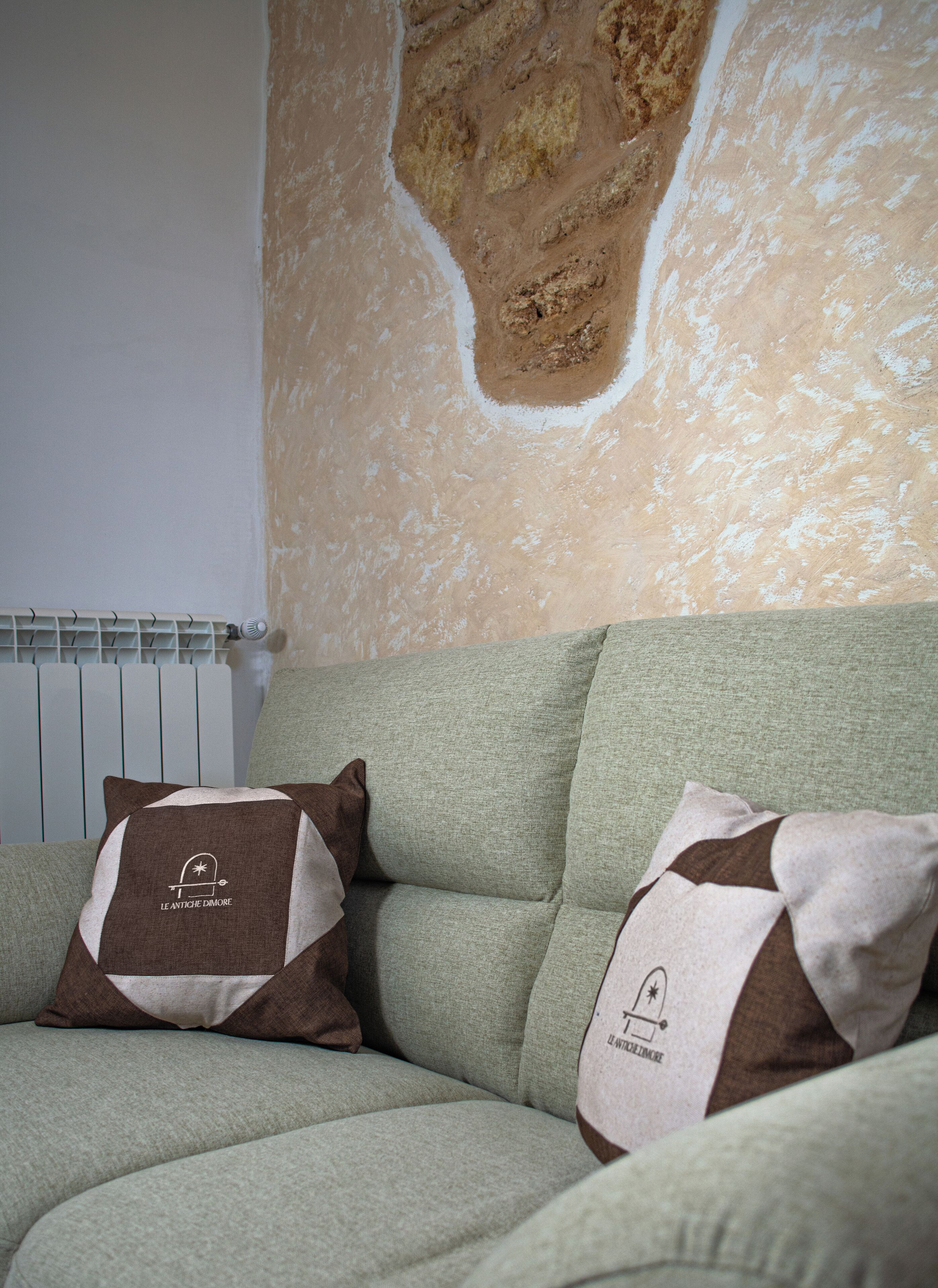 A green sofa with two pillows, one with a logo and text, and a radiator behind it.