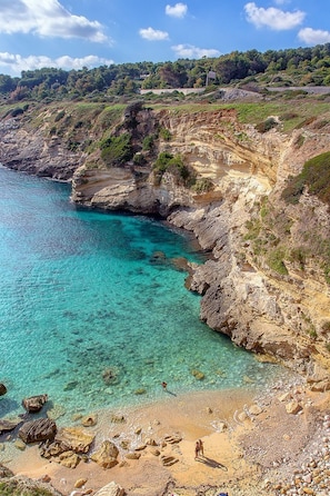 Un paisaje costero con aguas turquesas cristalinas, acantilados rocosos y una playa arenosa.