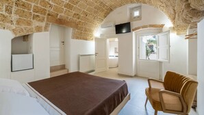 Un dormitorio con techo de piedra, una cama, una silla, un televisor y una puerta que da al baño.