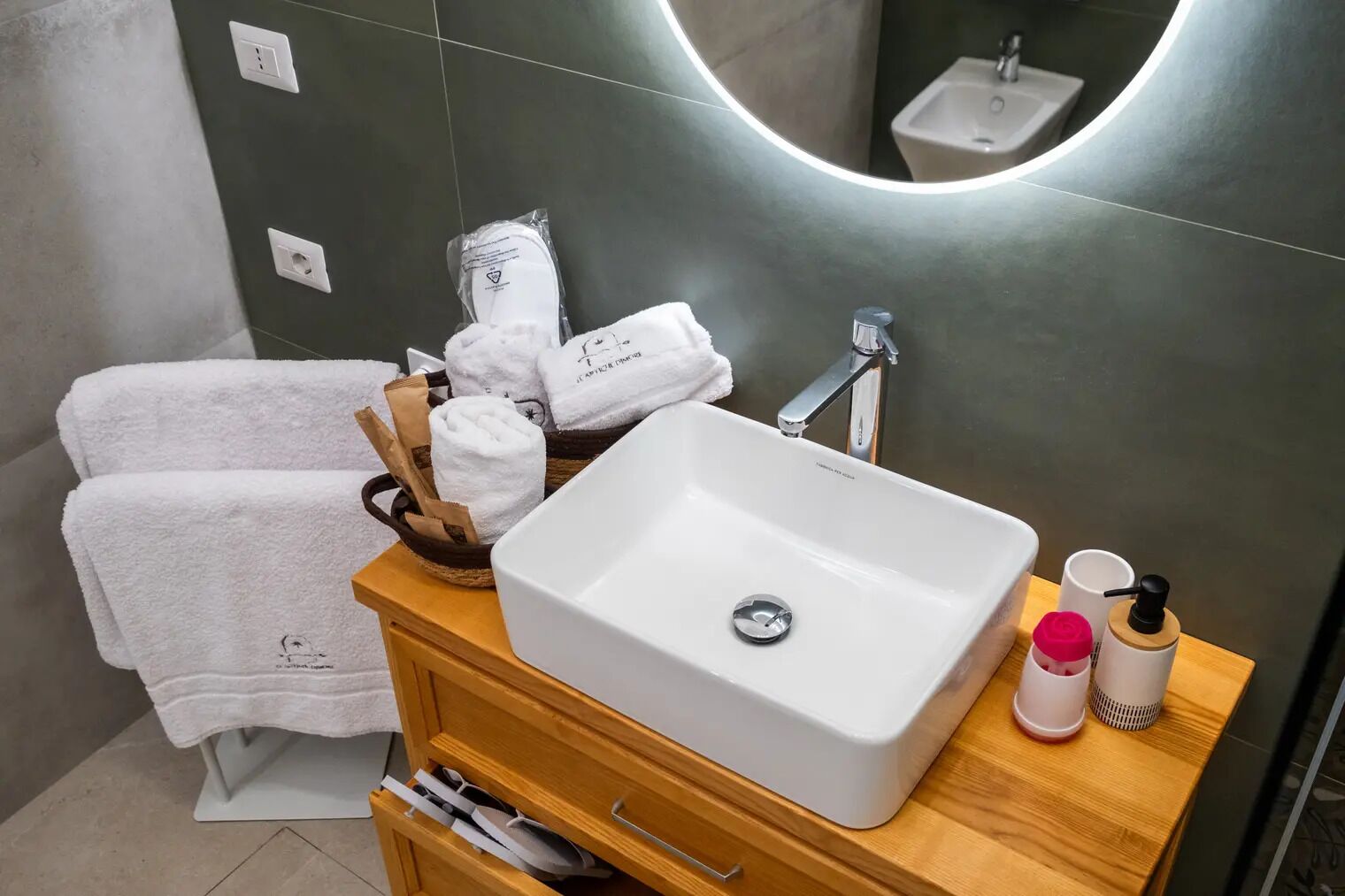 Un bagno con lavandino bianco, mobile contenitore in legno e specchio.