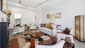 A spacious living room with a white sofa, a coffee table, and a fireplace. There is a large window providing natural light and a view of the outdoors. - Stylish Heritage Stay in Downtown Halifax (Halifax)