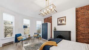 A modern bedroom with a bed, a desk, chairs, a fireplace, and large windows. - Stylish Heritage Stay in Downtown Halifax (Halifax)