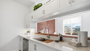 A modern kitchen with white cabinetry, a brick backsplash, a stainless steel sink, and a window with a view. - Stylish Heritage Stay in Downtown Halifax (Halifax)