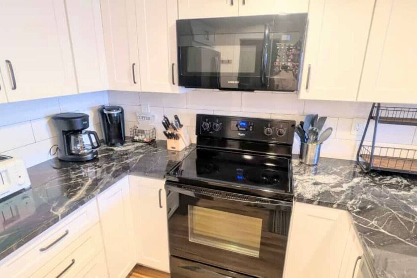 Uma cozinha com armários brancos, micro-ondas preto, forno duplo e cafeteira.