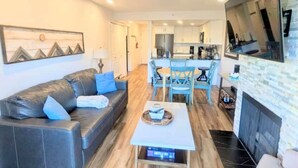 A modern living room with a leather sofa, a coffee table, and a dining area with blue chairs.