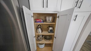 Una despensa de cocina con electrodomésticos de acero inoxidable, estantes de madera y diversos utensilios de cocina.